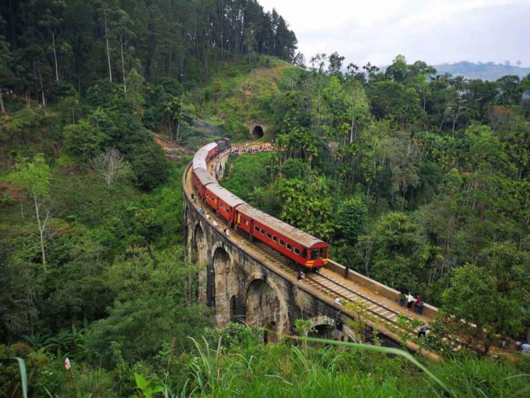 Train over the Nine Arches Bridge in Ella, surrounded by green hills.