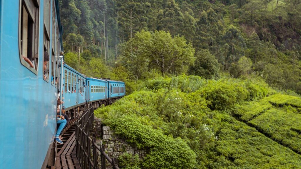 Train crossing the Nine Arch Bridge in Ella surrounded by lush green hills under misty skies
