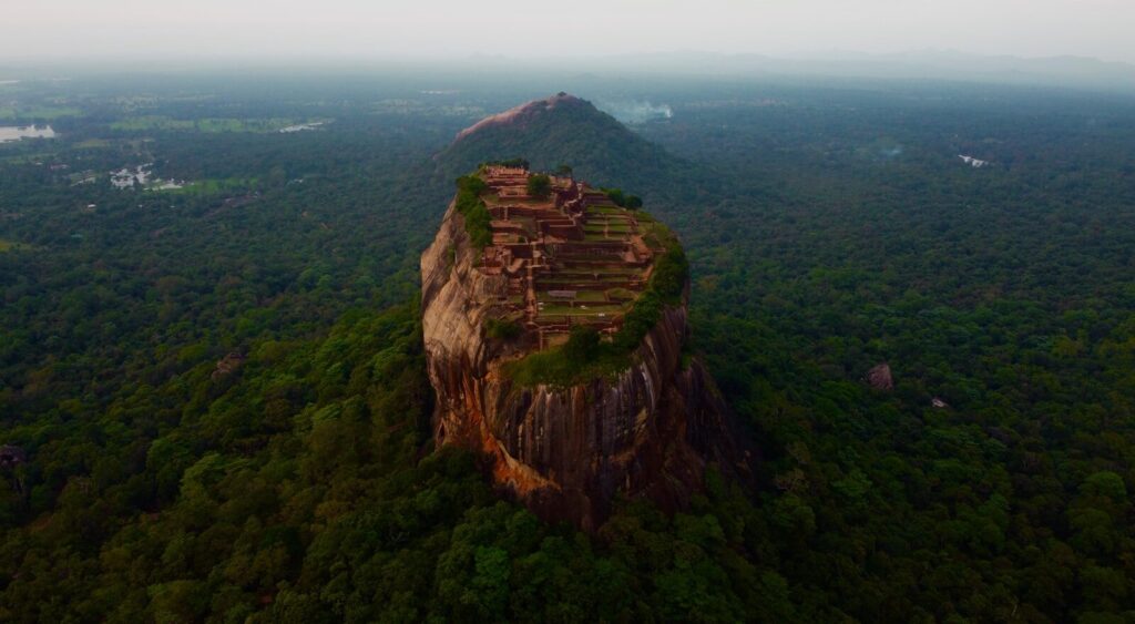 Sunrise view of Sigiriya Rock fortress from the summit of Pidurangala Rock with misty valleys below