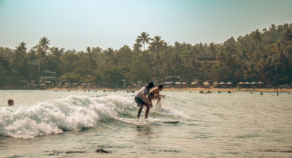 Surfer riding a wave on a sunny day at a palm-lined beach in Sri Lanka — supporting travel image 3