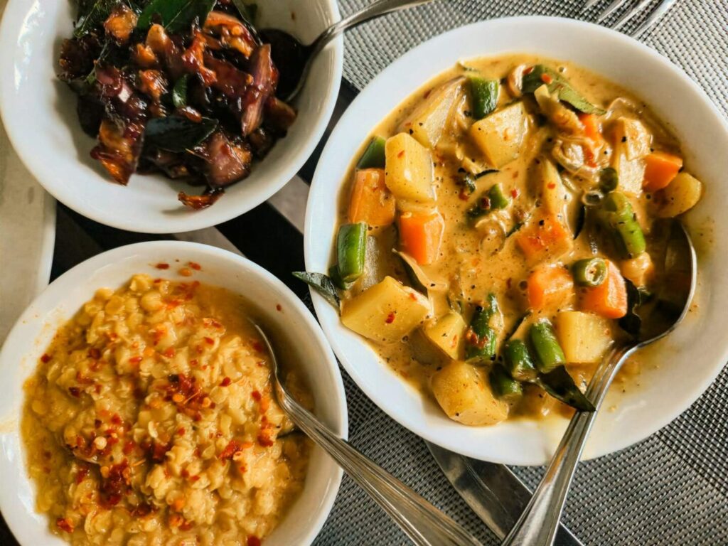 A colorful plate of Sri Lankan rice and curry with various vegetable and meat curries alongside traditional condiments — supporting travel image 2